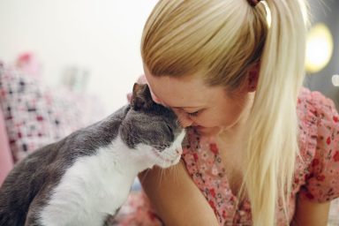 A blonde woman cuddling with a grey and white cat, looking content and happy.