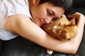 Close-Up Of Smiling Woman With Cat Lying On Sofa At Home
