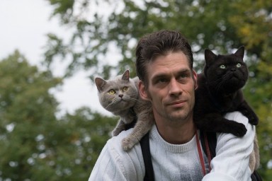 Male on a bike with 2 cats enjoying the ride on his shoulder.