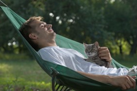 A man lying in a hammock petting a cat
