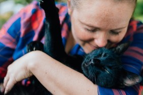 Portrait of blondhaired woman hugging her black cat outdoor.