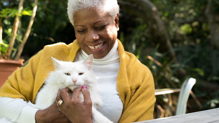 A senior woman sits in the garden cuddling a beautiful white cat.