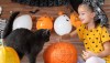 Girl in witch halloween costume sitting on a table playing with pumpkin and her pet cat. Halloween lifestyle background.
