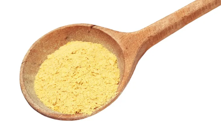 Nutritional yeast flakes in a wooden spoon isolated on white with clipping path included.