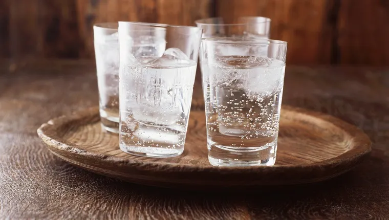 Sparkling water in drinking glass with ice on vintage wooden plate