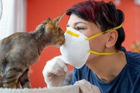 Mid Adult Female Pet Owner Kissing Her Cat With Protective Mask During Coronavirus Pandemic.