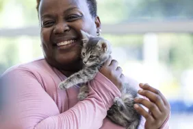 Woman wearing pink shirt cuddling with a rescue kitten.