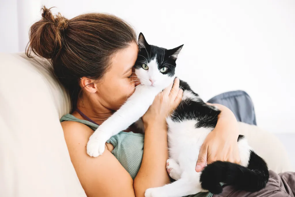 Woman snuggling a black and white cat on the couch.