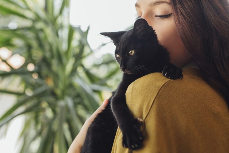 woman holding black cat on shoulder