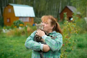 older woman kissing cat with farm in background